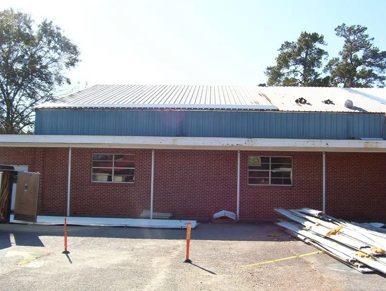 The same building mid metal roof installation, materials staged on the ground and an older roof section still exposed